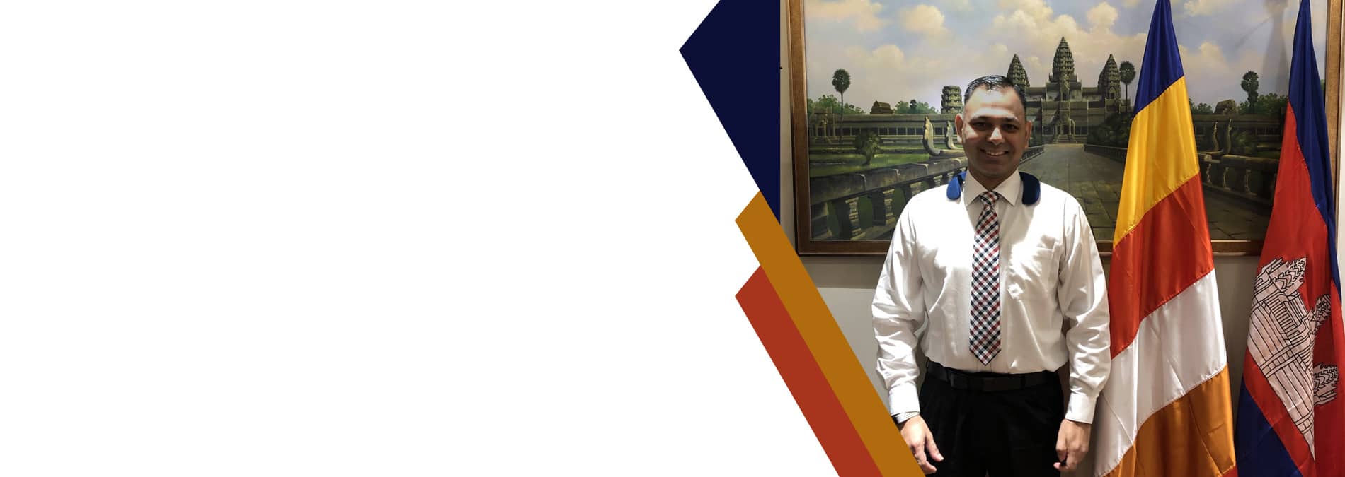 Amit Suden standing beside flags and a painting of Angkor Wat